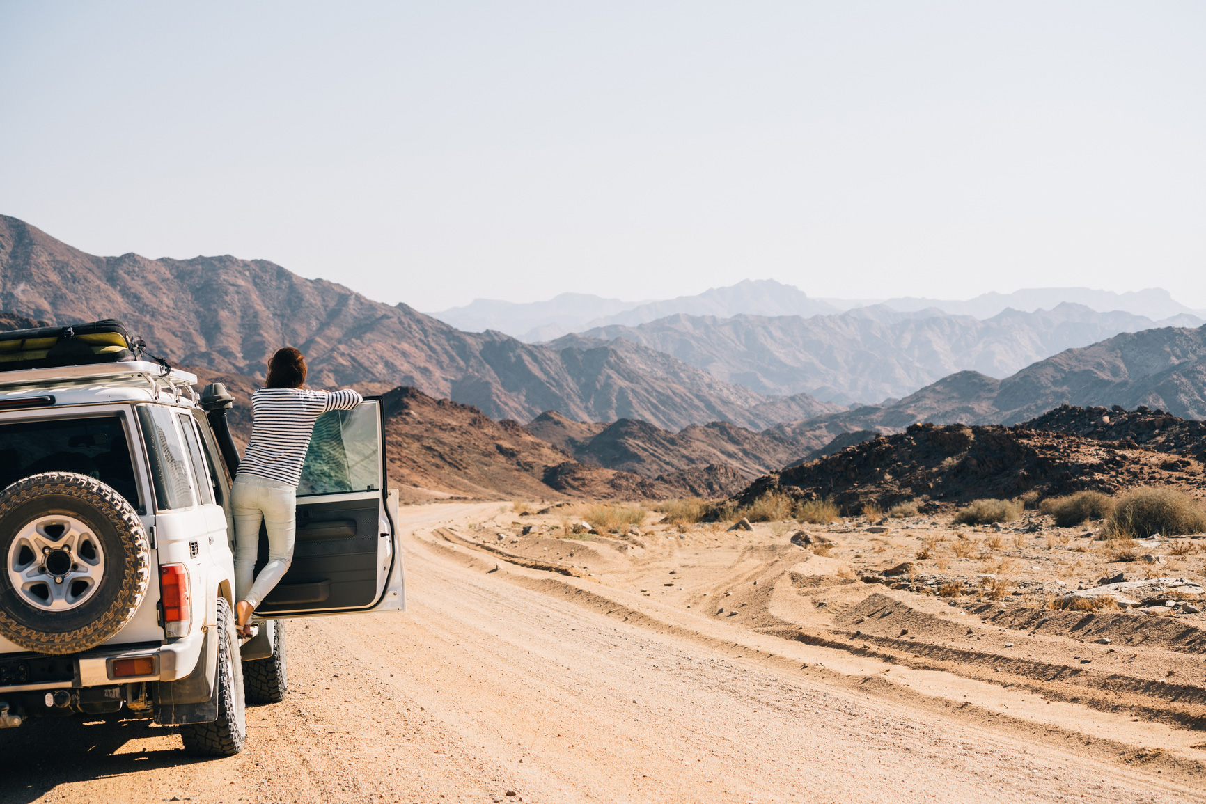 Woman leaning out of the door to a jeep on a dirt road in the desert.