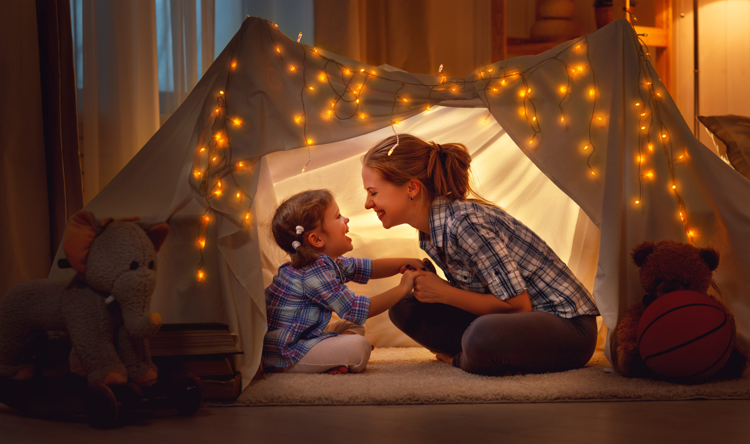 A mother and daughter sitting in an indoor tent that is covered in small lights. 